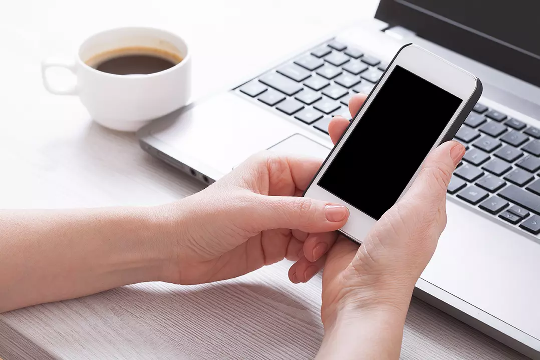 Persona frente a laptop, celular y café, apple presenta iOS 14