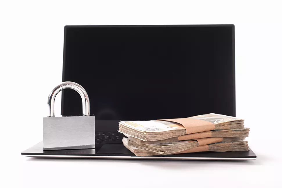 Computadora abierta y sobre el teclado un candado y dos fajos de dinero, represetnando los ataques de malware a instituciones de gobierno que han aumentado