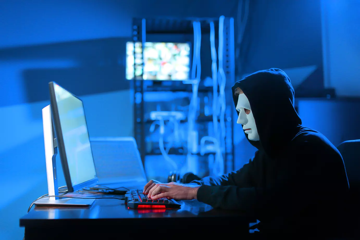 Hacker con mascara blanca frente a una computadora. Representando el ataque con ransomware que resulta en secuestro de los sistemas de ciudad española