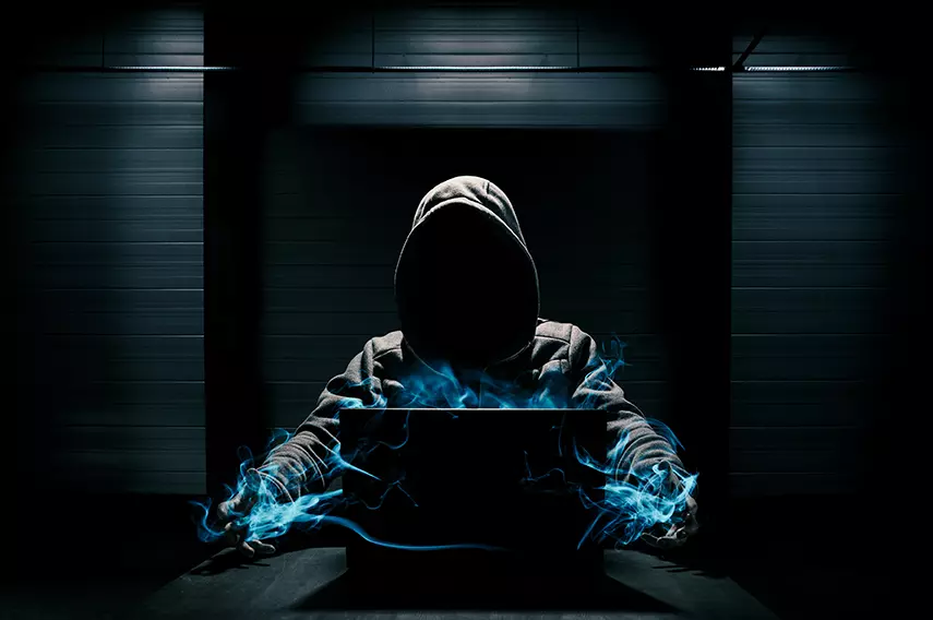 Fondo oscuro de un hombre con sudadera frente a una computadora, representando a hackers rusos tramando ciberataques en contra de juegos olímpicos Tokio