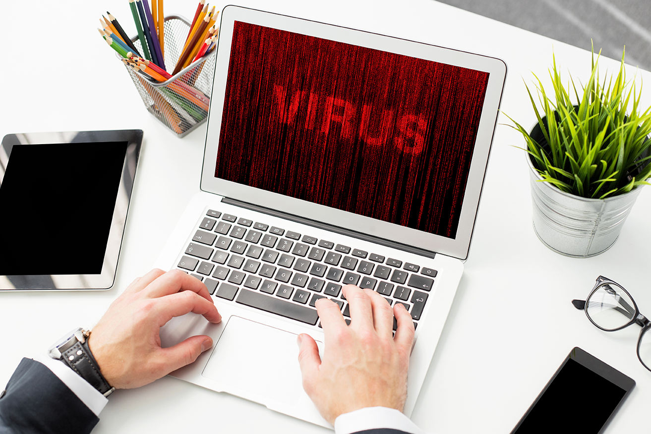 Hombre frente a su computadora sobre escritorio y en la pantalla se observa el letrero de VIRUS en color rojo, así como muchos de los nuevos sitios sobre el coronavirus son maliciosos.