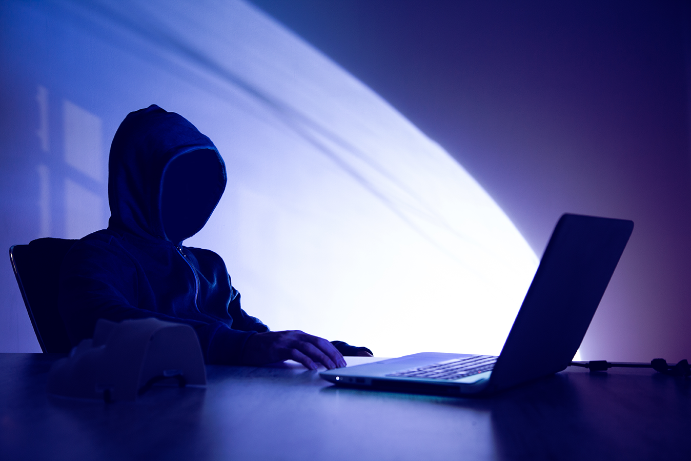 fondo oscuro con persona con apariencia de hacker frente a una computadora sobre un escritorio simulando un hacker con la noticia que una mujer muere a causa de un ciberataque en Alemania