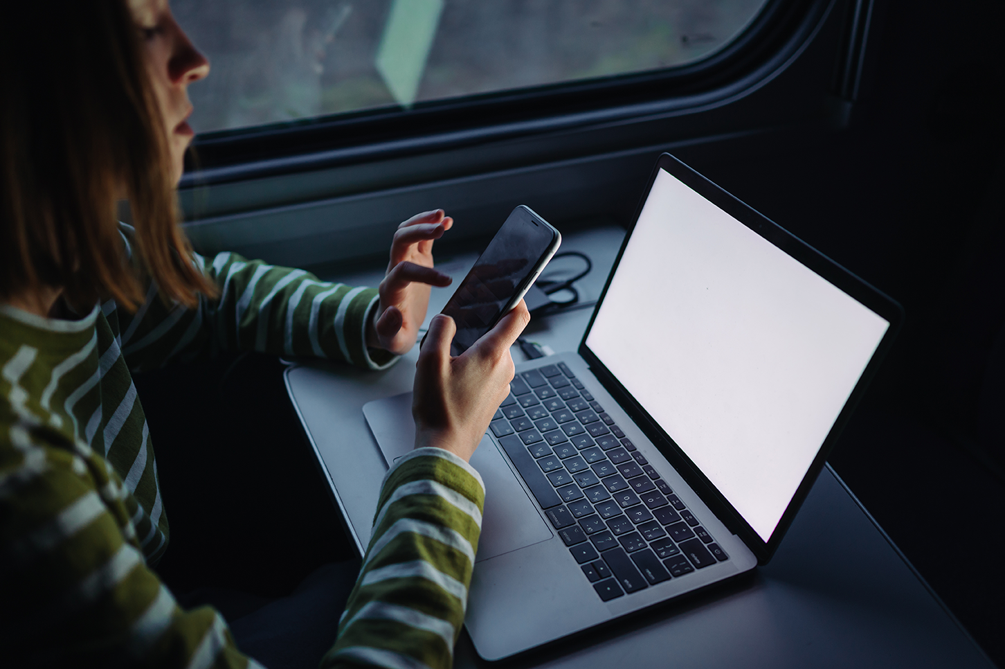 Mujer frente a laptop y celular, wifi gratuito de estaciones de tren británicas