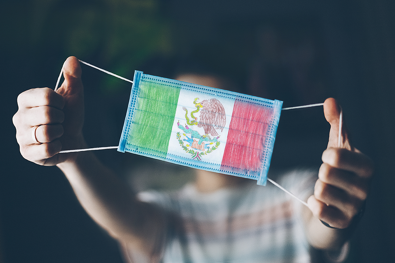 Persona de fondo mostrando un cubrebocas con la bandera de México mostrando el COVID-19 en México la evolución de la contingencia y el impacto económico