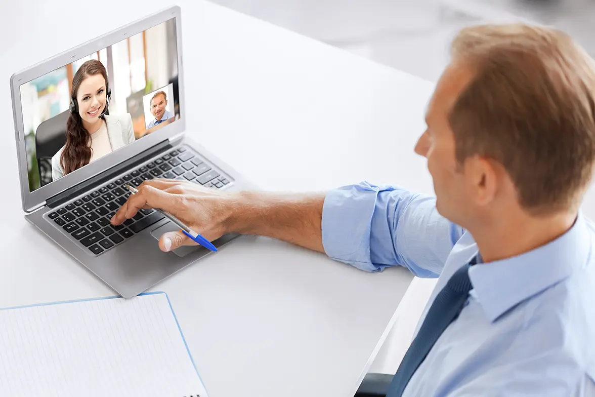 Hombre ejecutivo frente c computadora sobre escritorio teniendo una videoconferencia. sigue los consejos para tener una mejor videoconferencia desde casa.