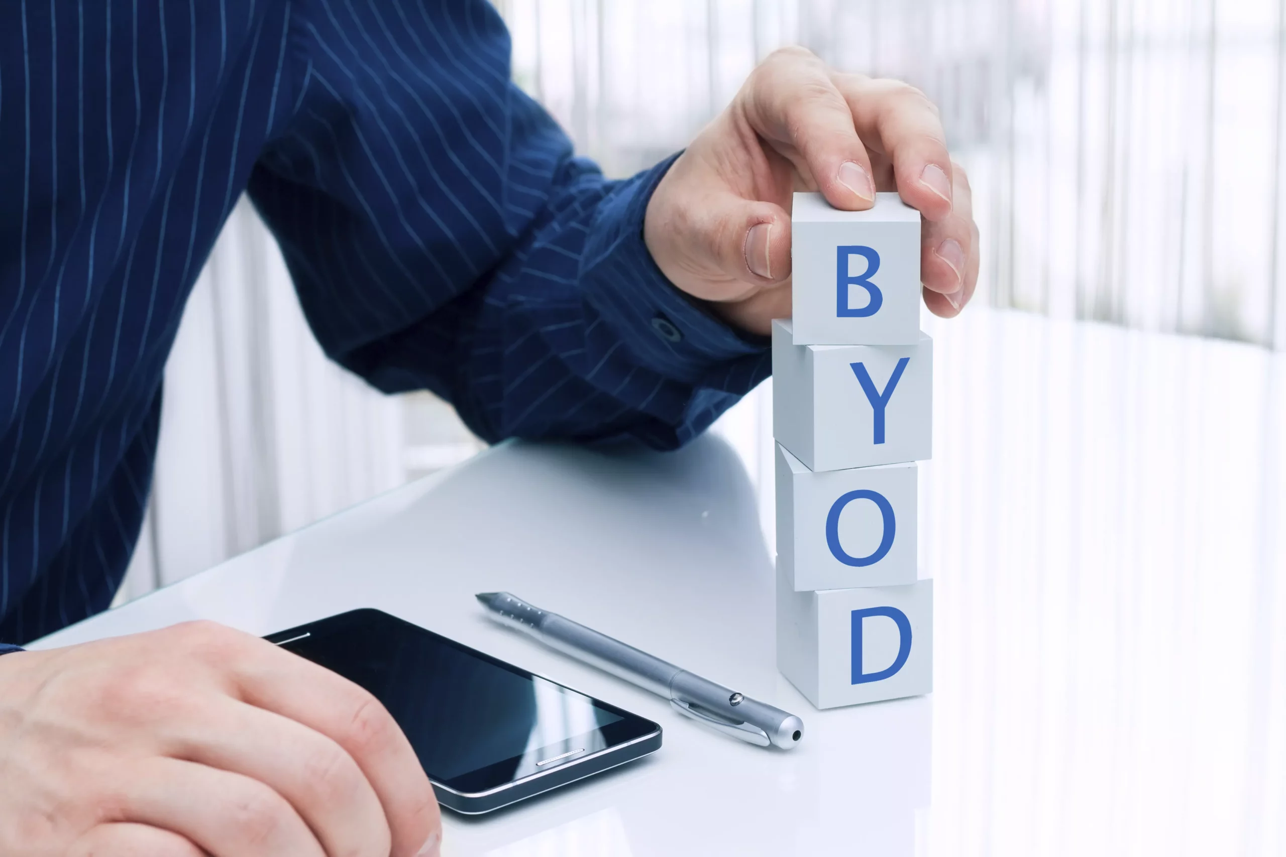 Ingeniero recargado en un escritorio con un celular y una torre de dados con las iniciales BYOD. Mostrando las ventajas y desventajas de una política BYOD