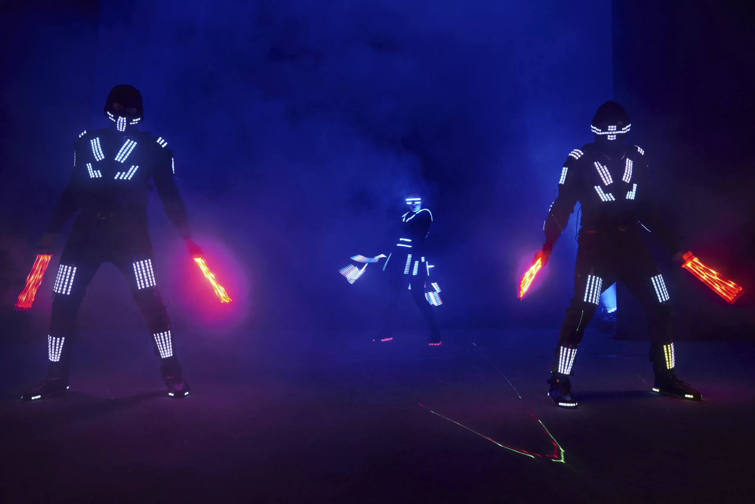 3 personas con apariencia de robot y luces con fondo negro, representando a los robots de Boston Dynamics que ya pueden bailar
