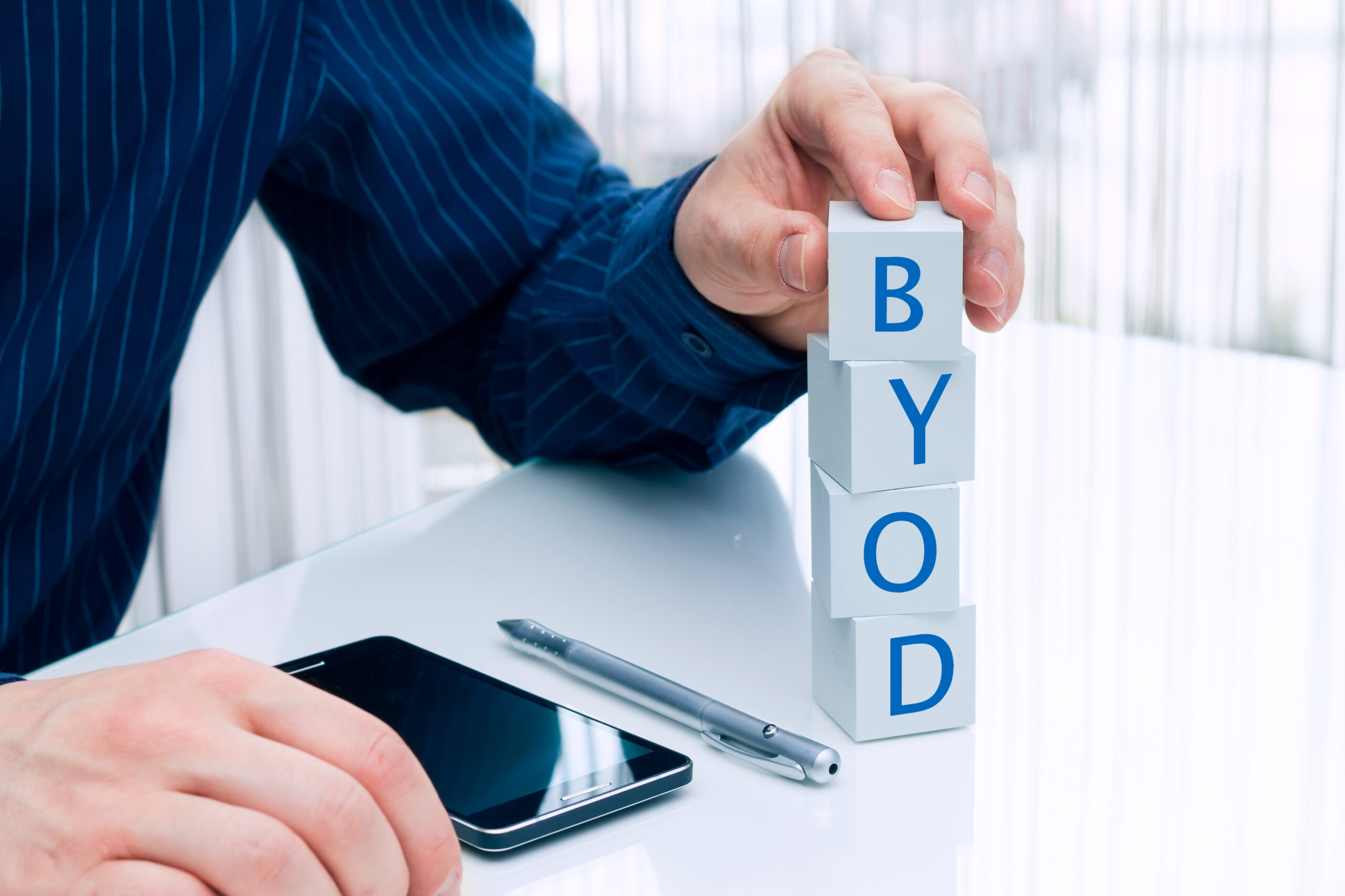 Ejecutivo recargado en un escritorio con un celular y colocando bloques con las iniciales BYOD revisando el top5 trends que definirán el futuro de los endpoint de aquí en adelante