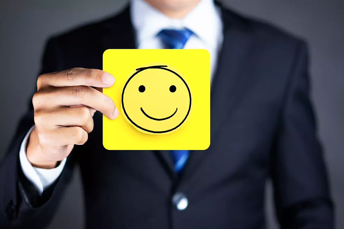 Hombre con traje mostrando un cuadro con una carita feliz de color amarillo representando los 4 aspectos clave de la actitud de servicio