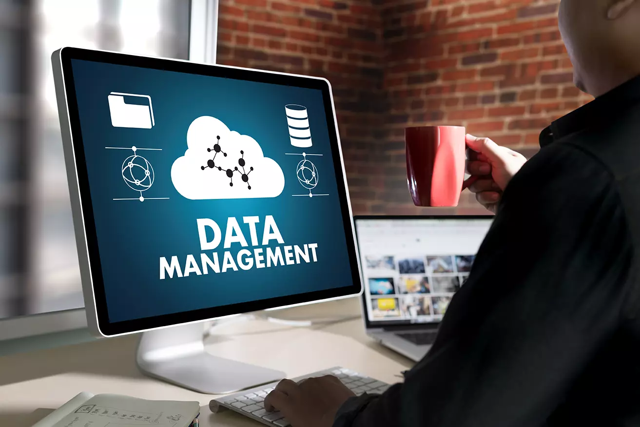 Hombre frente a computadora en el monitor aparece una nube con la palabra data management mostrando 4 razones para automatizar la ingesta de datos