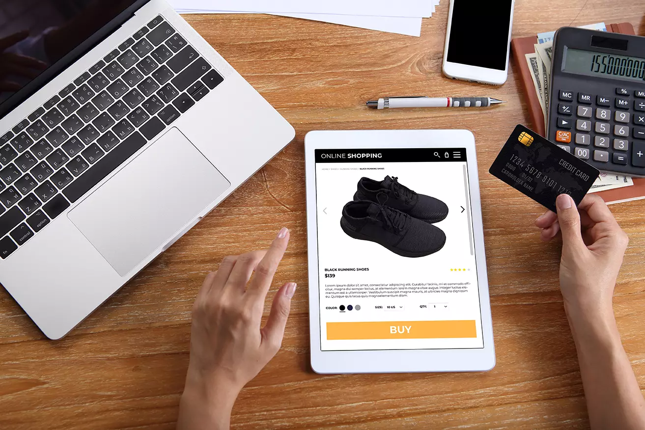 sobre escritorio una computadora y una tablet, persona comprando online mediante la aplicación de realidad aumentada de Nike que permite medir los pies para vender los tenis correctos.