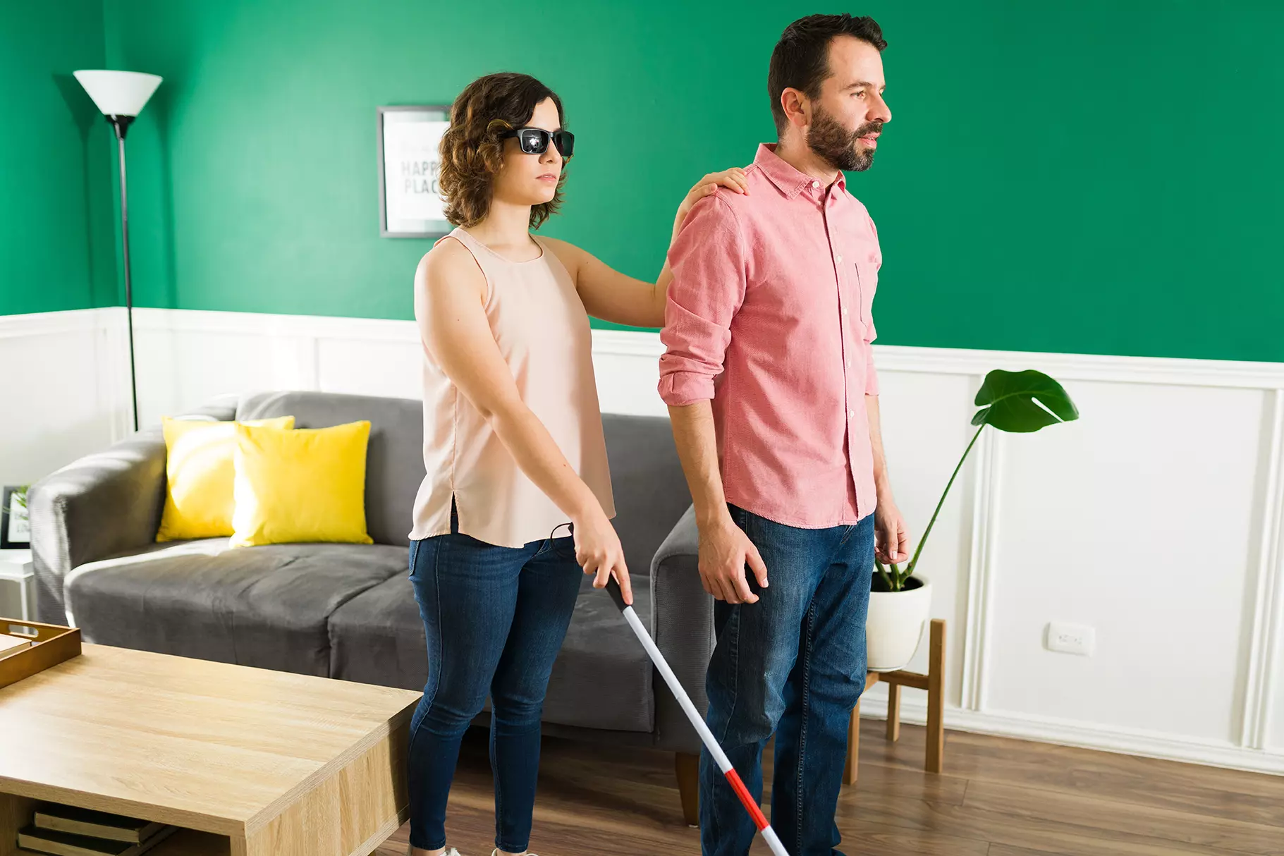 Mujer con debilidad visual apoyándose de un bastón y del hombro de un hombre en la sala representando a CARA, el asistente de realidad aumentada para ciegos.