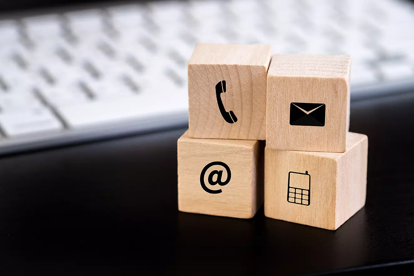 Cuadritos de madera a lado de teclado blanco que contienen iconos de un teléfono y correo