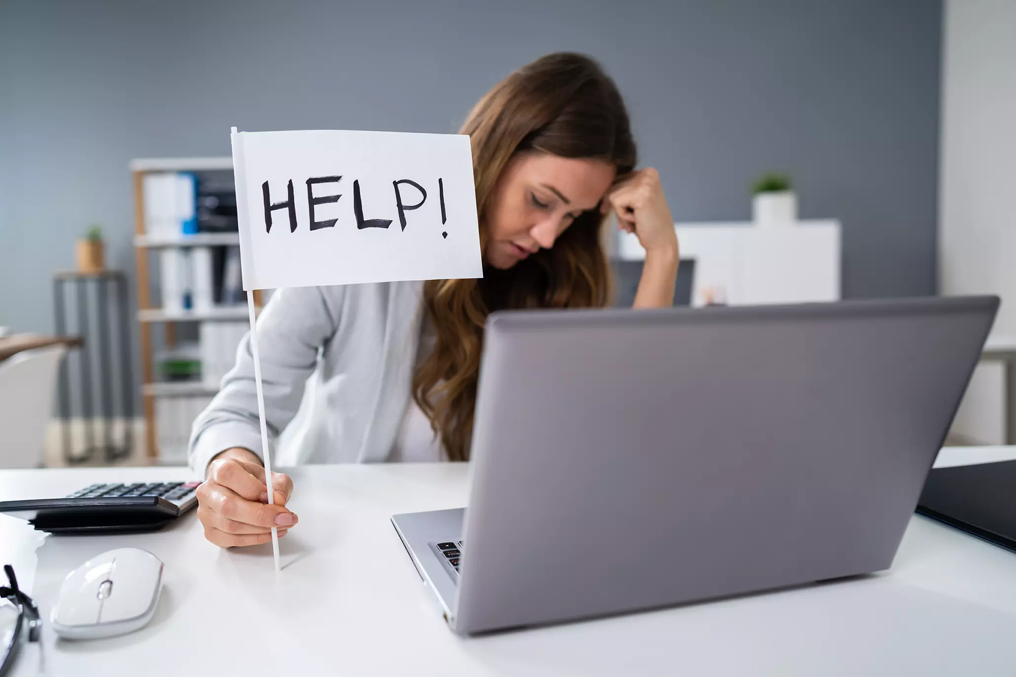 Mujer frente a la computadora abrumada con un letrero de ayuda mostrando cómo mejorar la salud mental del equipo de soporte de TI