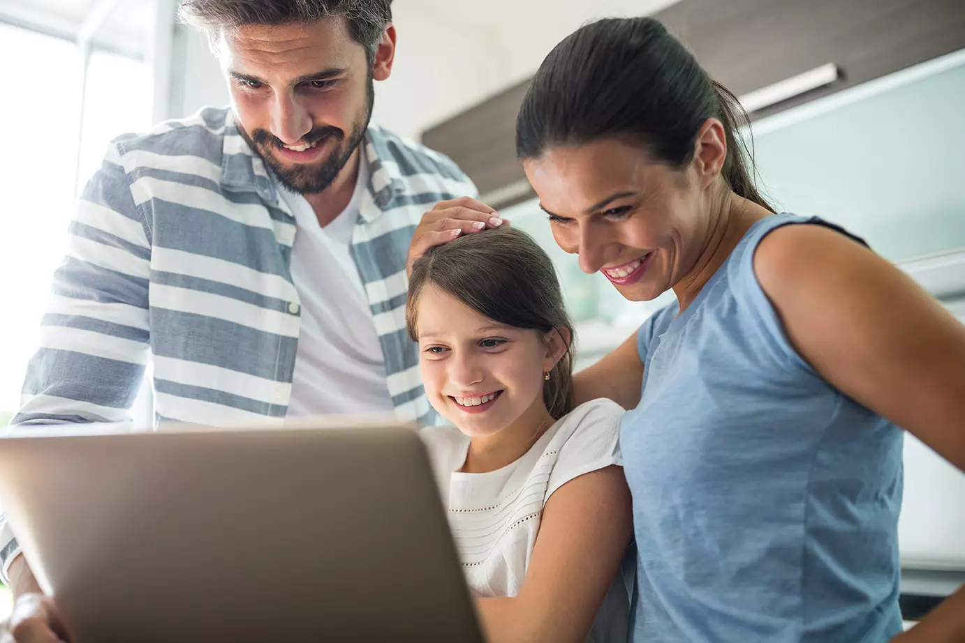 Papas con su hija frente a una computadora mostrando como el Family Link de Google permite a los padres controlar el uso del teléfono de sus hijos.
