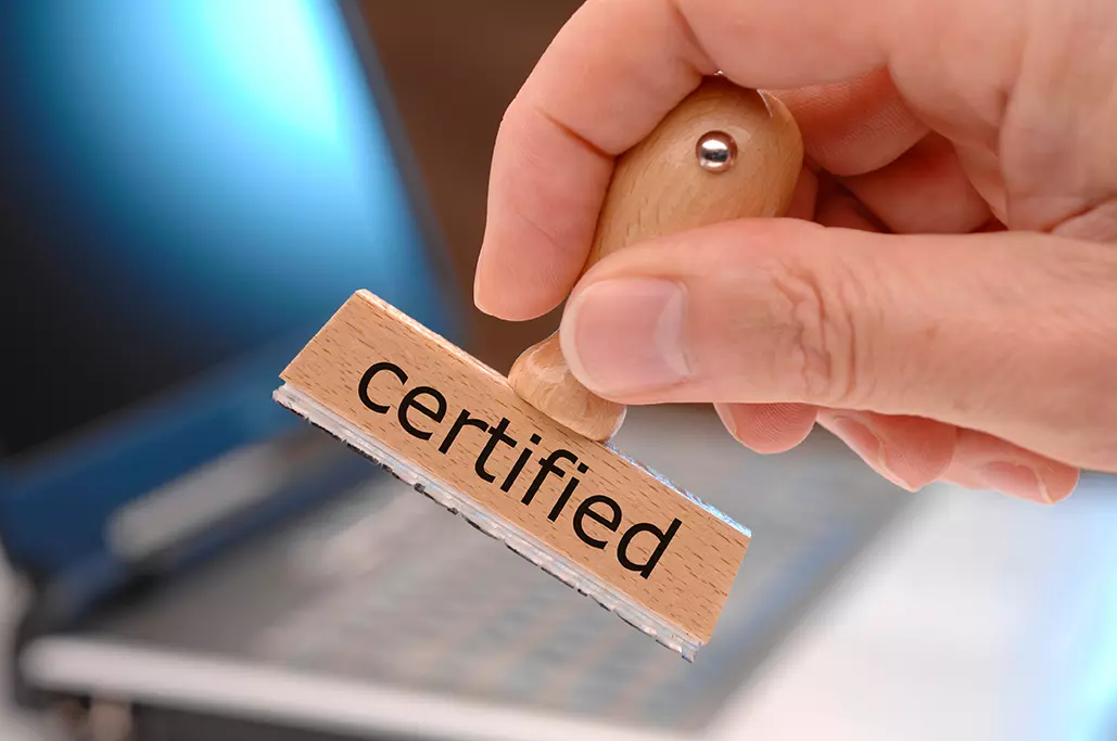 Computadora de fondo y en primer plano persona con sello de certified indicando que Fortinet ofrece certificaciones gratuitas en ciberseguridad