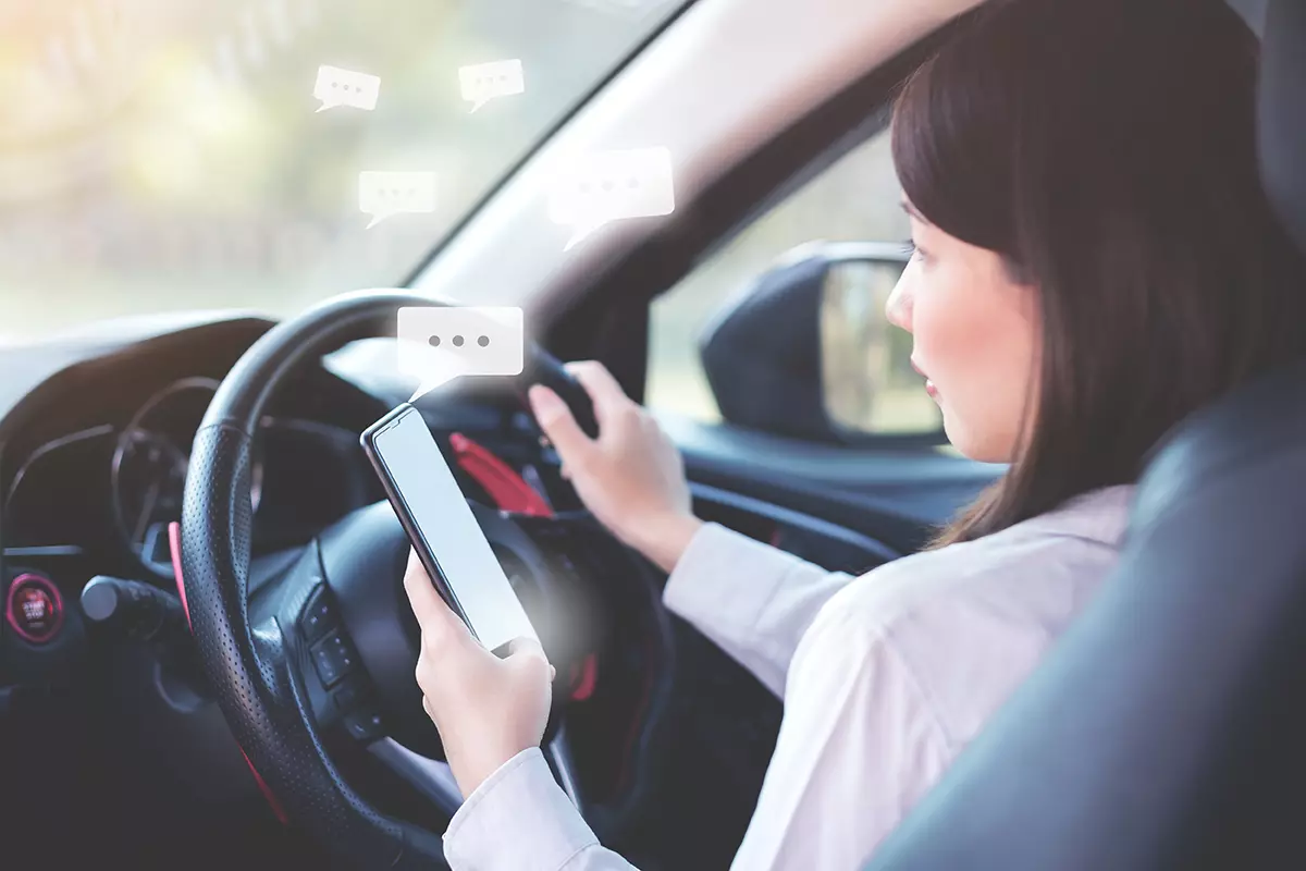 Mujer utilizando celular manejando su auto revisando como Uber ofrece solución para usuarios que no desean charlar con el conductor