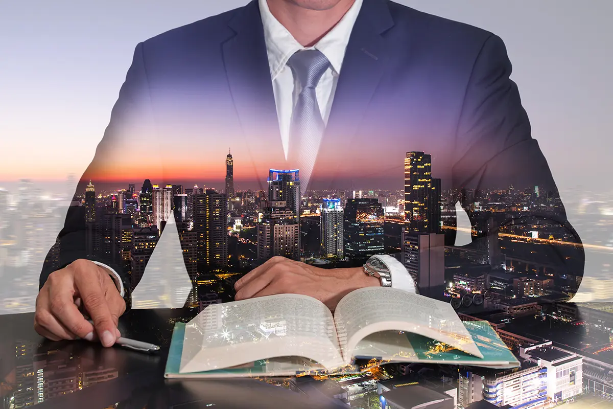 Hombre con traje leyendo un libro con imagen traslucida de una ciudad mostrando 3 lecturas para que tu empresa crezca aceleradamente.
